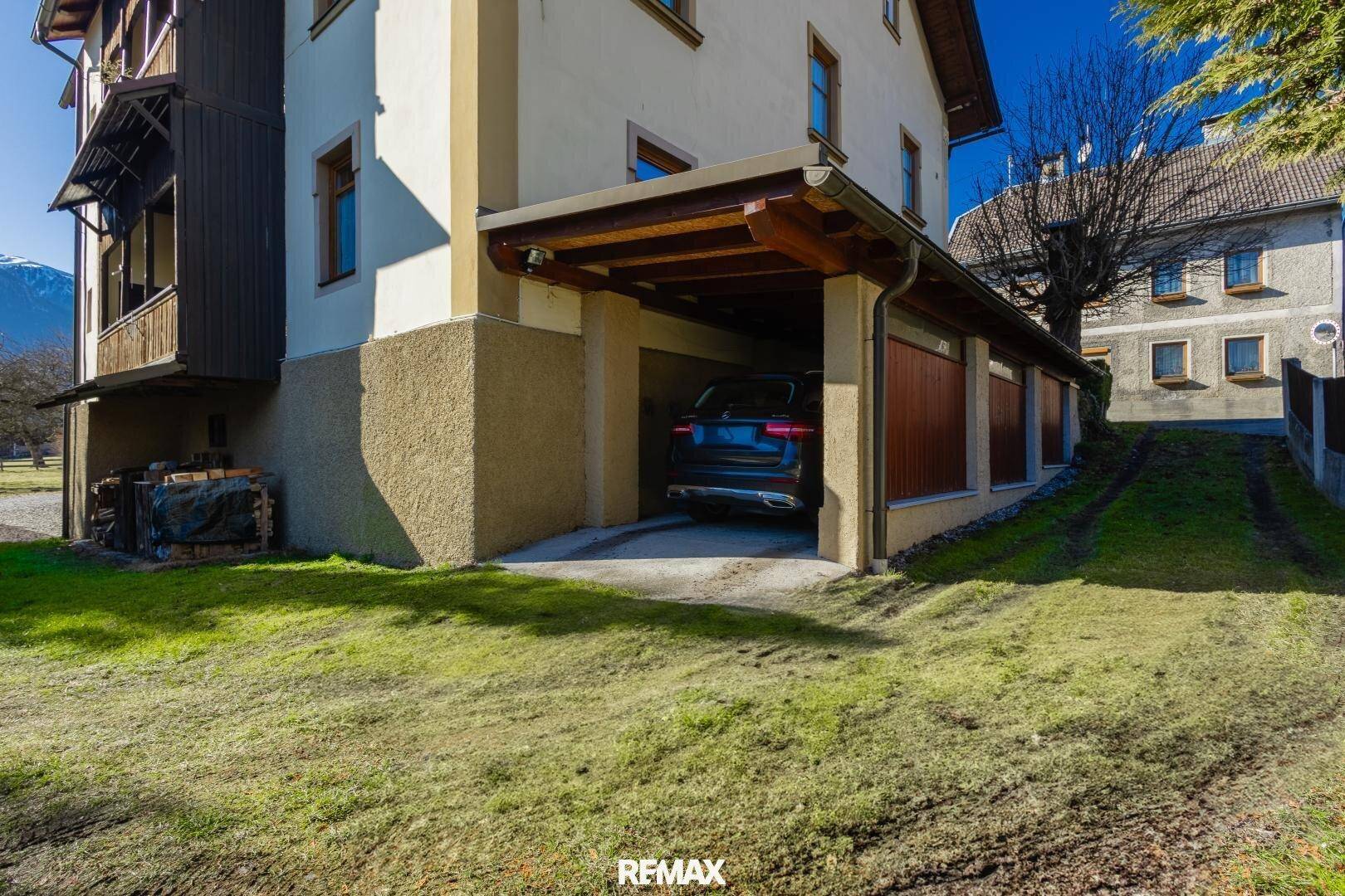 Hausfassade mit integriertem Carport und gepflegtem Rasen, umgeben von Natur.