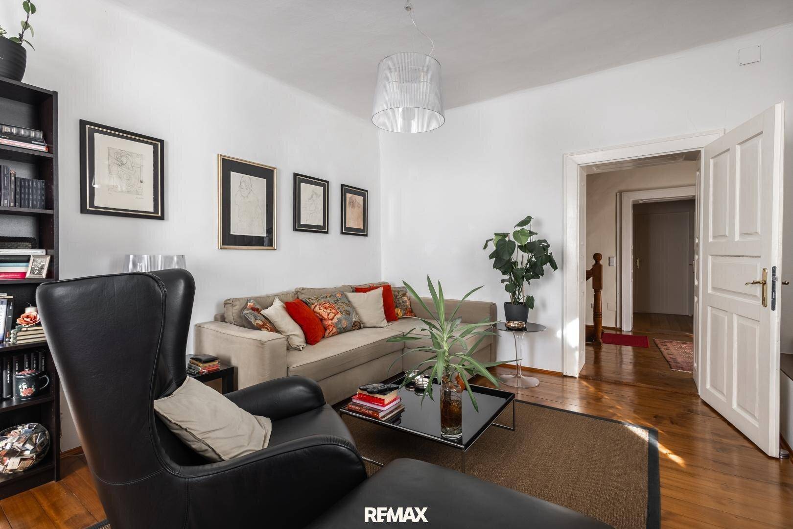 Helles Wohnzimmer mit beigem Sofa, schwarzem Sessel und Holzboden, ideal zum Entspannen.