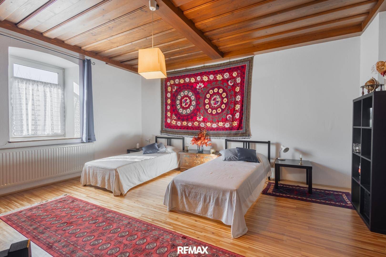 Gemütliches Schlafzimmer mit zwei Einzelbetten, Holzbalkendecke und traditionellem Teppich.