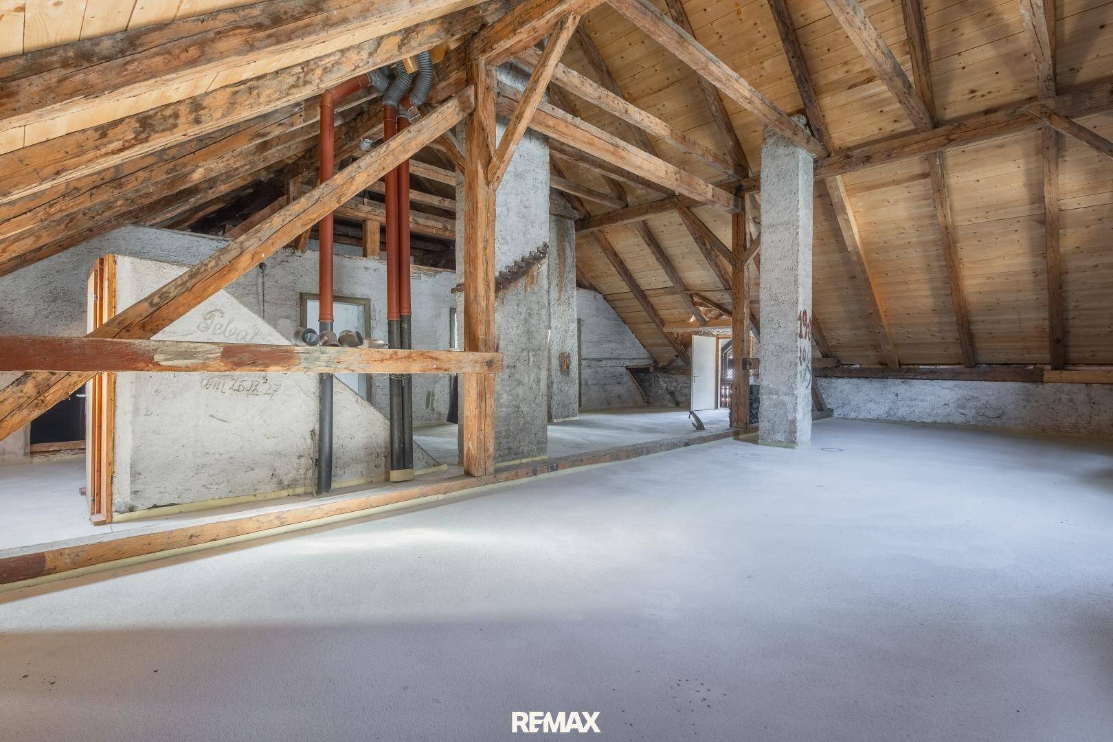 Unausgebauter Dachboden mit sichtbaren Holzbalken und Betonboden, bereit für den Ausbau.