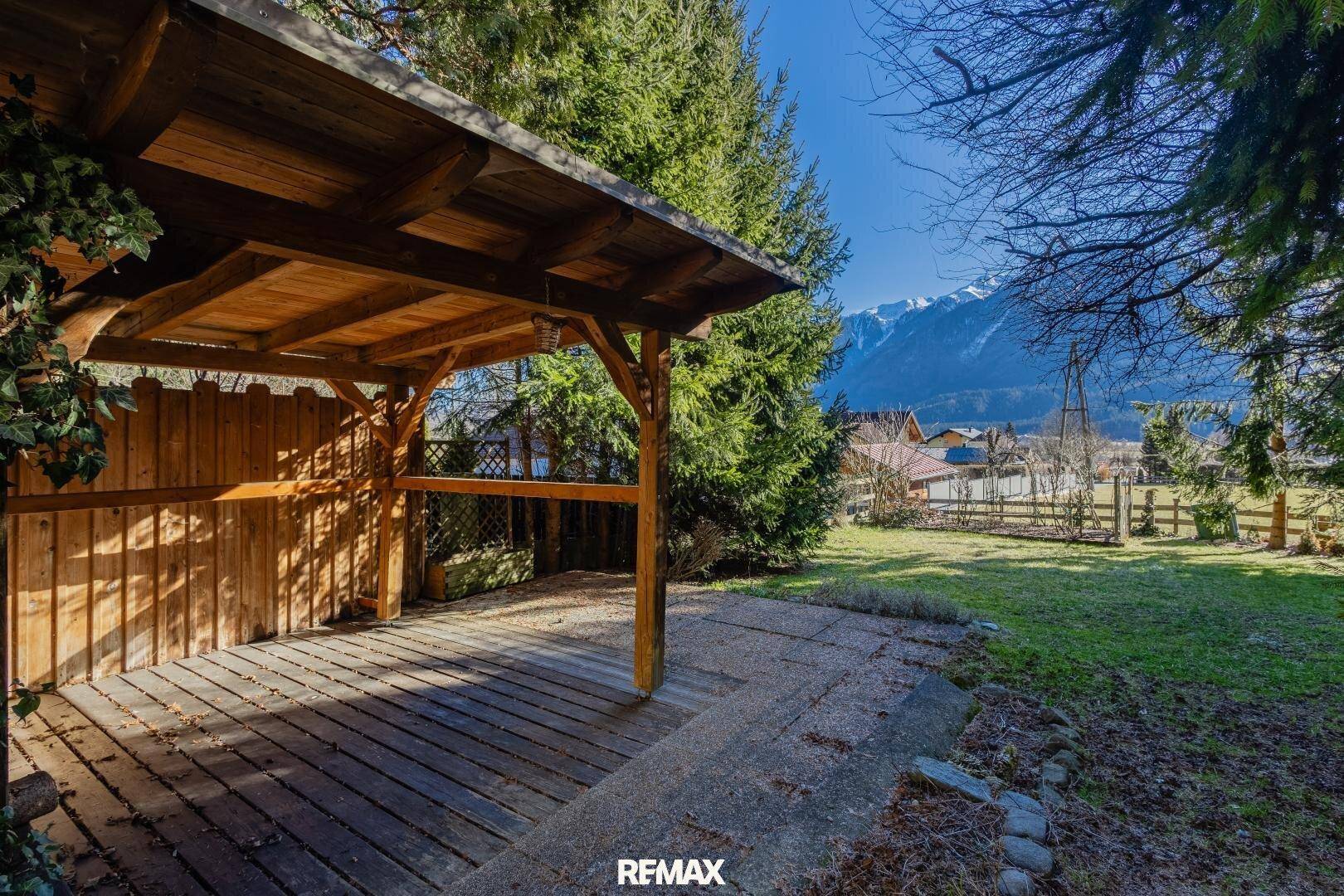Überdachter Sitzbereich im Garten mit Holzboden und weitem Blick auf die Berge.