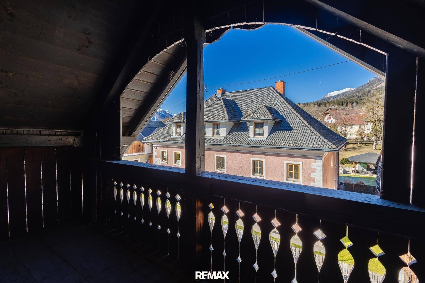 Traditioneller Holzbalkon mit geschnitztem Geländer und Blick auf ein charmantes Nachbarhaus.
