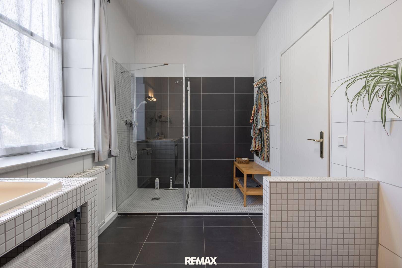 Helles Badezimmer mit großer begehbarer Dusche, dunklen Akzentfliesen und Fenster für Tageslicht.