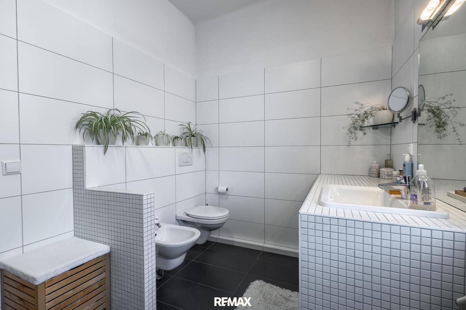 Modernes Badezimmer mit weißen Fliesen, Bidet und Einzelwaschbecken, hell und funktional gestaltet.