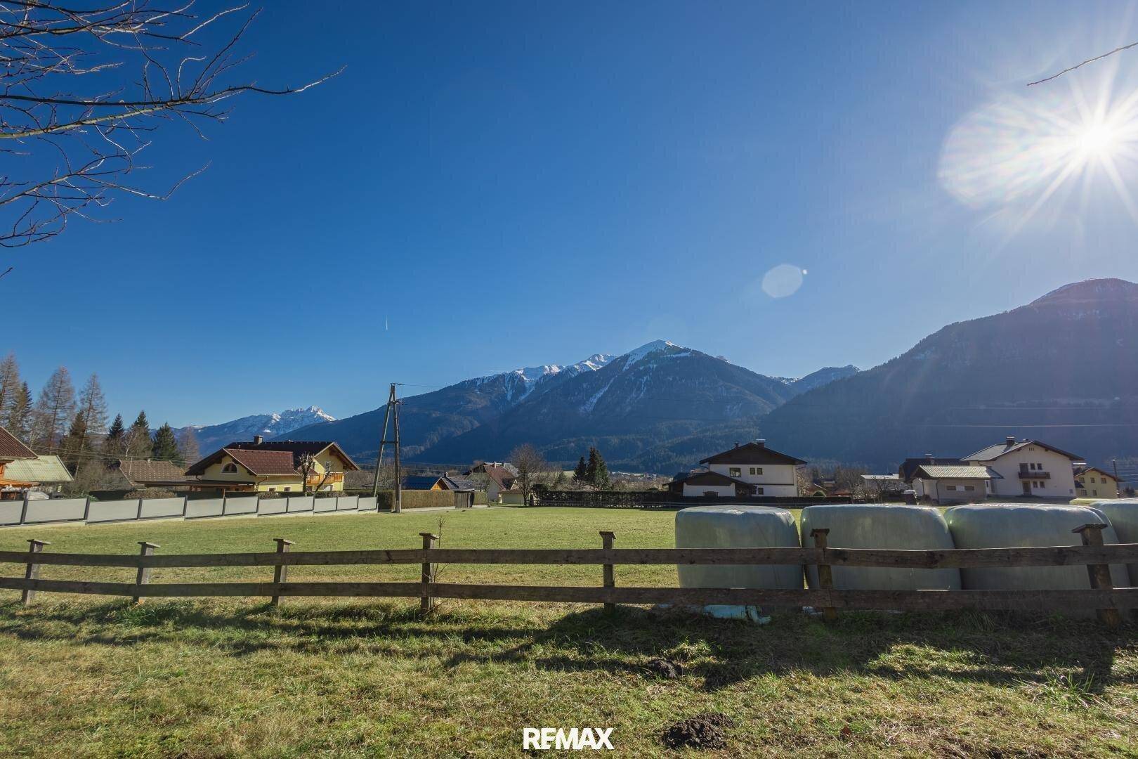 Malerische Landschaft mit weiten Feldern, schneebedeckten Bergen und strahlend blauem Himmel.
