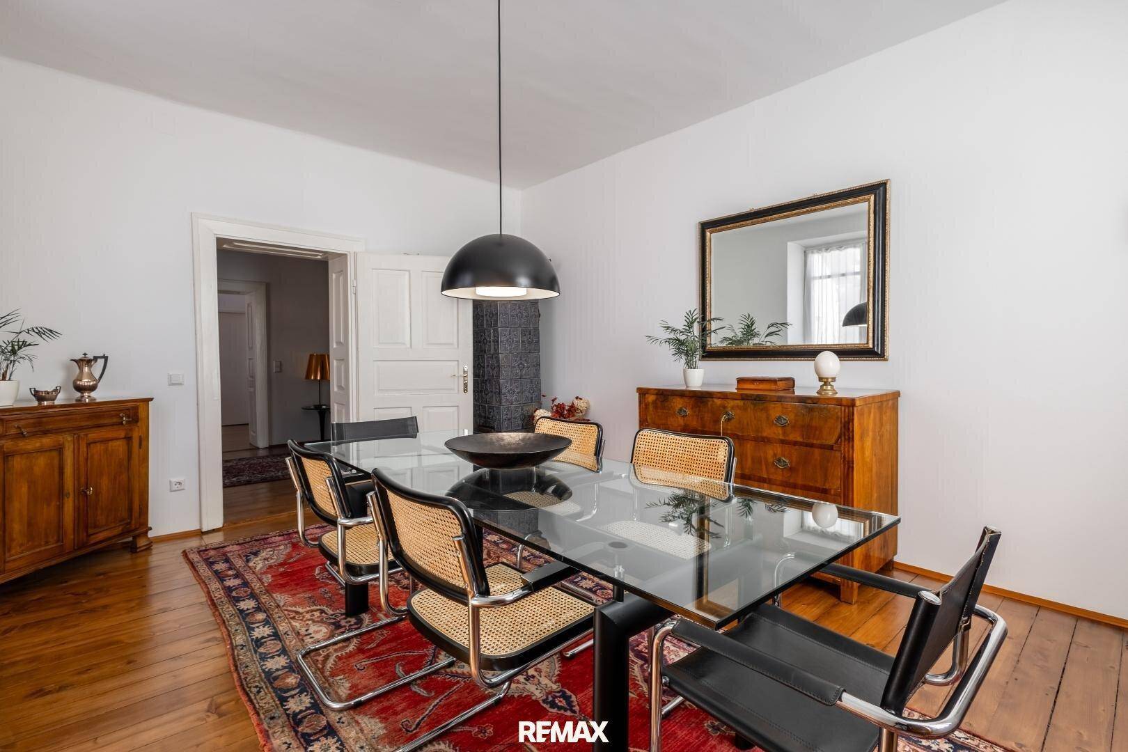 Eleganter Essbereich mit Holzboden, modernem Glastisch und klassischen Stühlen, ideal für gesellige Runden.