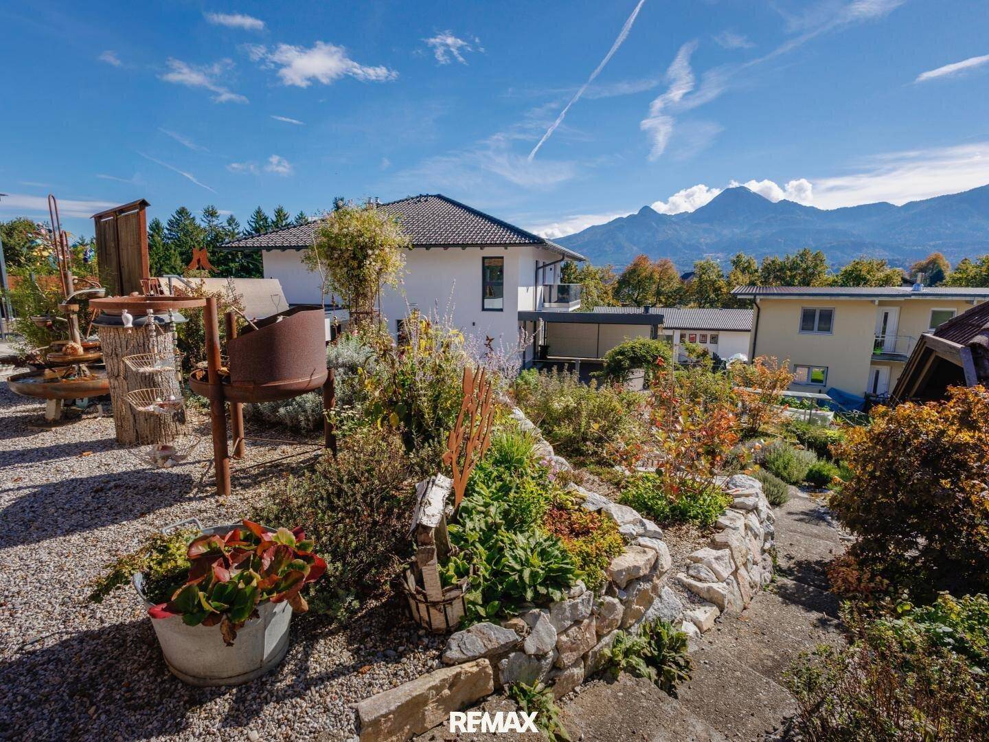 Mediterraner Gartenbereich mit Steinmauern und vielfältiger Bepflanzung, im Hintergrund die majestätische Bergkulisse.