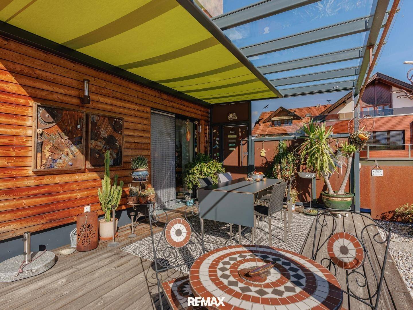 Überdachte Terrasse mit Esstisch und dekorativen Pflanzen, perfekt für Mahlzeiten im Freien.