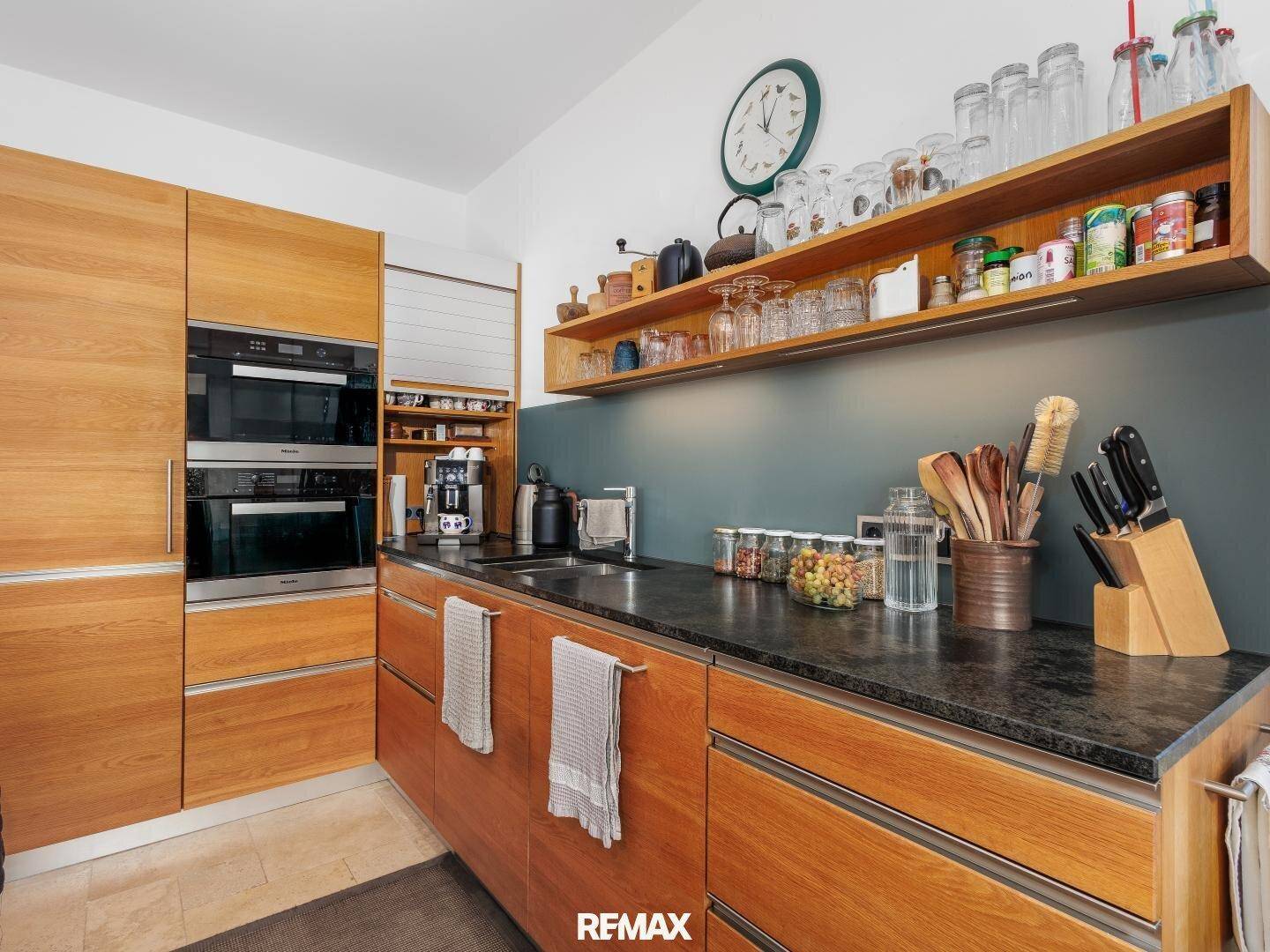 Moderne Einbauküche mit Holzfronten, dunkler Arbeitsplatte und integrierten Geräten.
