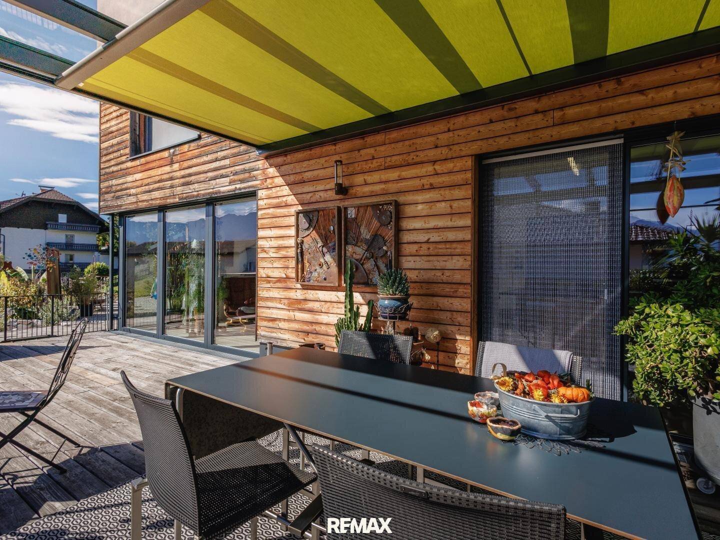 Helle, überdachte Terrasse mit großem Esstisch und Blick ins Grüne, ideal für gesellige Runden.