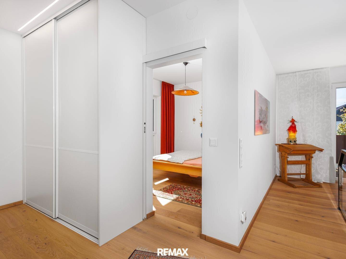 Moderner Flur mit weißem Schiebeschrank und Zugang zu einem farbenfroh dekorierten Schlafzimmer.