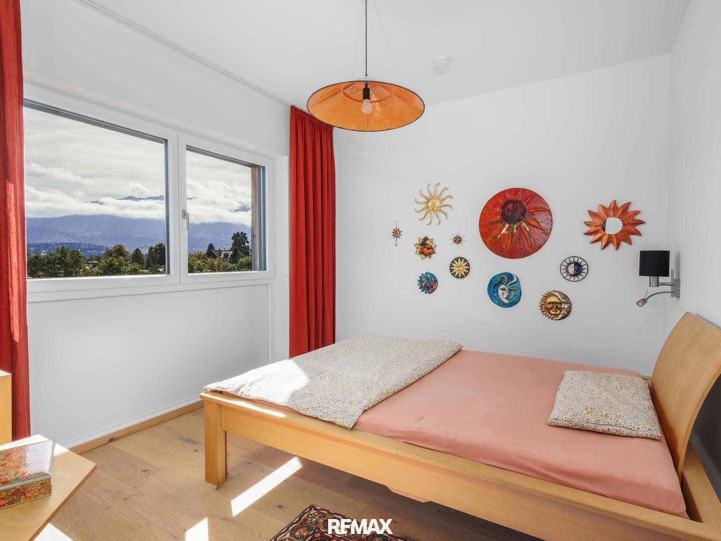 Freundliches Schlafzimmer mit Holzbett, farbenfroher Wanddekoration und Panoramablick auf die Berge.