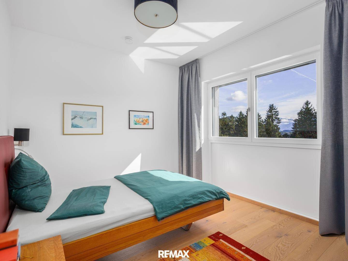 Helles Schlafzimmer mit Holzbett, Parkettboden und weitem Blick auf die umliegende Natur und Berge.