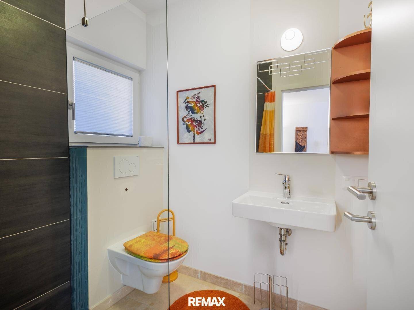 Modernes Badezimmer mit Toilette, Waschbecken und Duschbereich hinter einer Glaswand.
