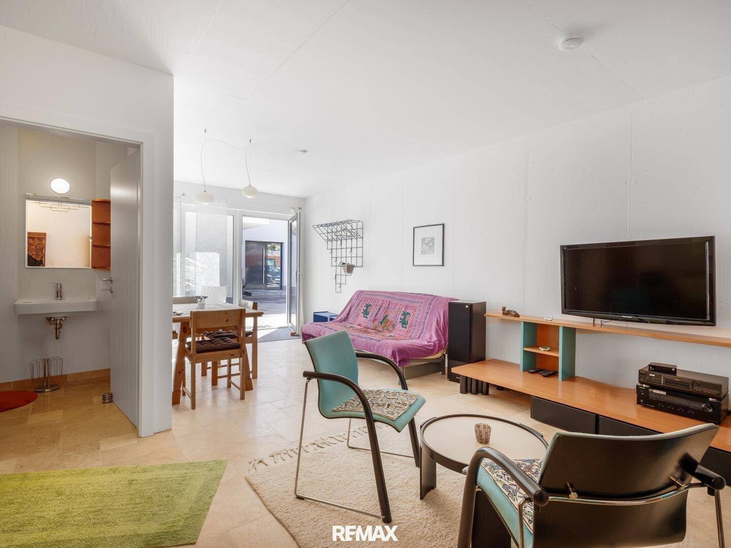 Wohnbereich mit Sofa, Fernseher und Esstisch, mit Zugang zu einem Außenbereich.