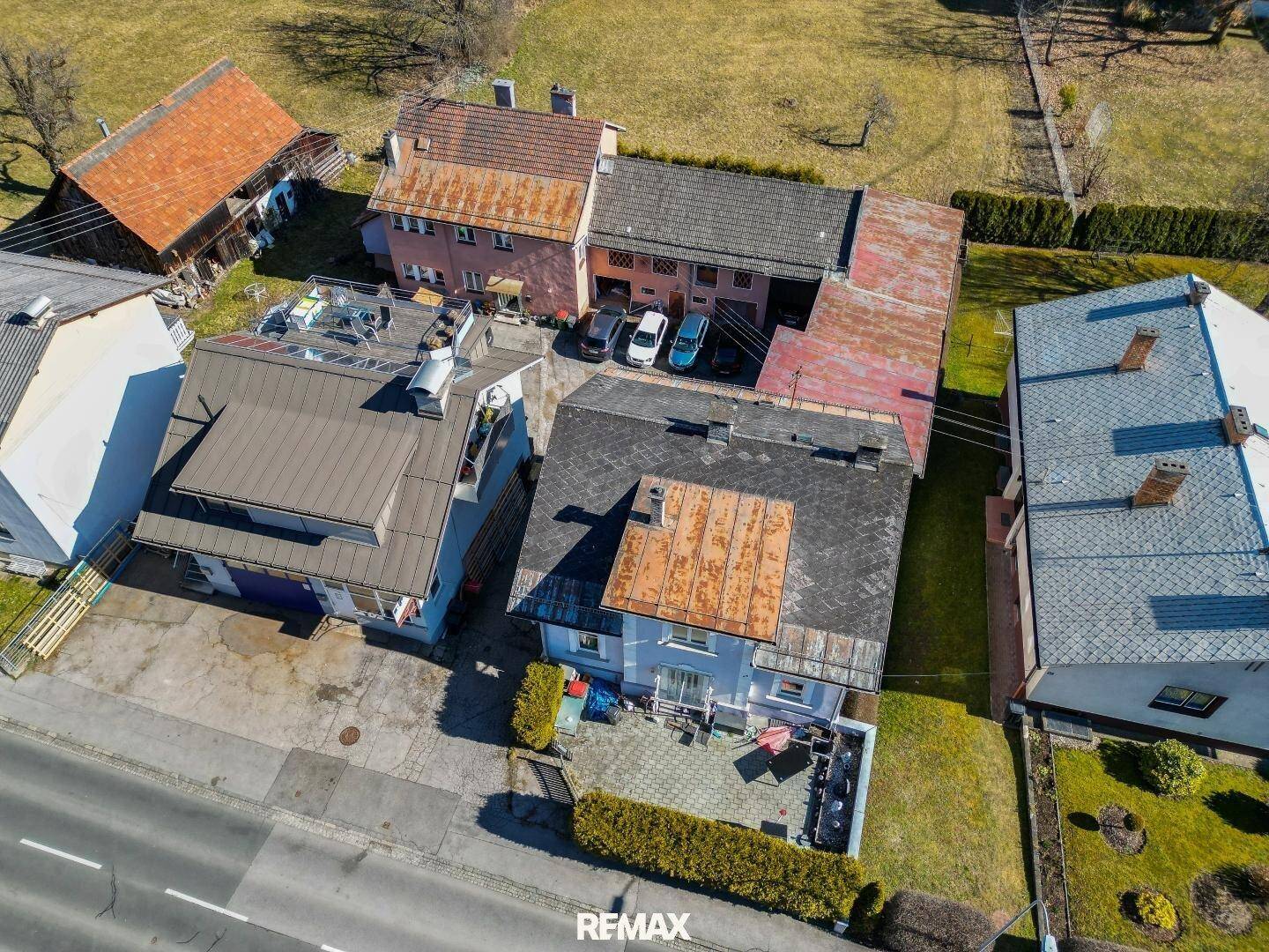 Schrägansicht aus der Luft zeigt das Anwesen mit Terrasse, Garagen und umliegenden Häusern.