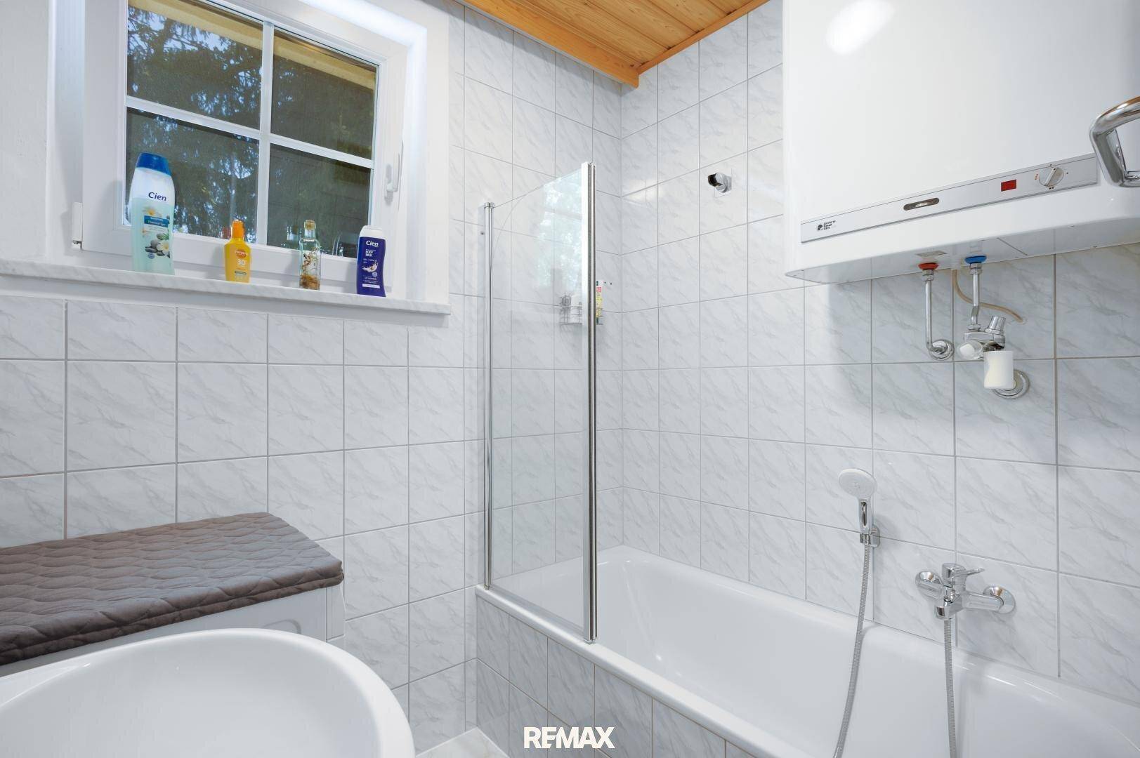 Badezimmer mit Badewanne, Duschabtrennung und Fenster für Tageslicht.