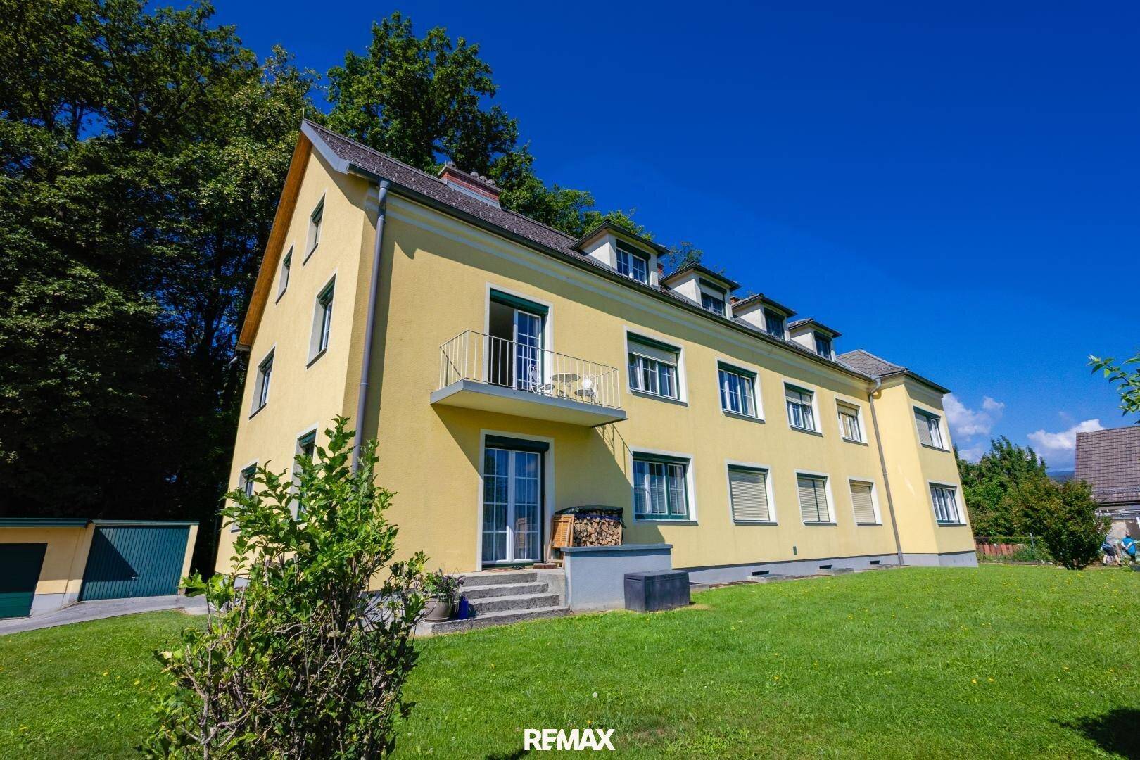 Ansicht des gelben Gebäudes mit Balkon und Zugang zum Gartenbereich.