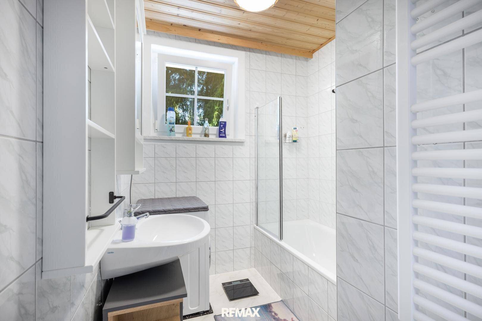 Modernes Badezimmer mit Badewanne, Duschwand und beheiztem Handtuchhalter, hell gefliest.