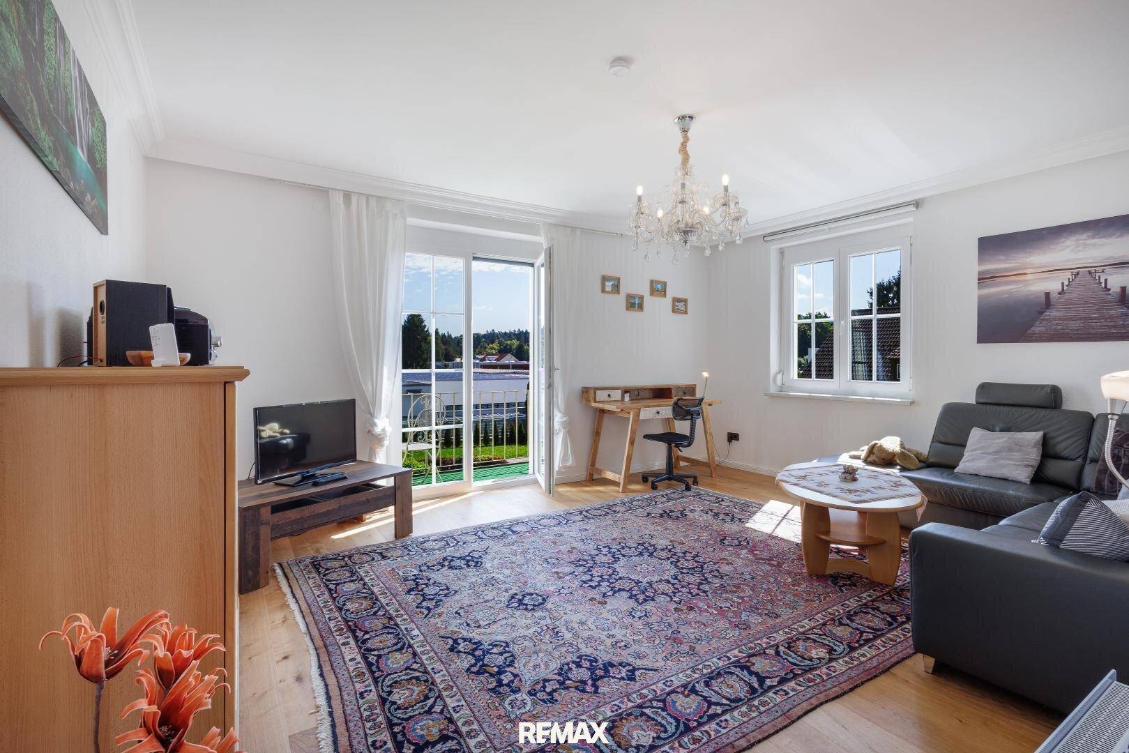 Gemütliches Wohnzimmer mit Holzboden, großem Teppich und Zugang zu einem Balkon mit Weitblick.