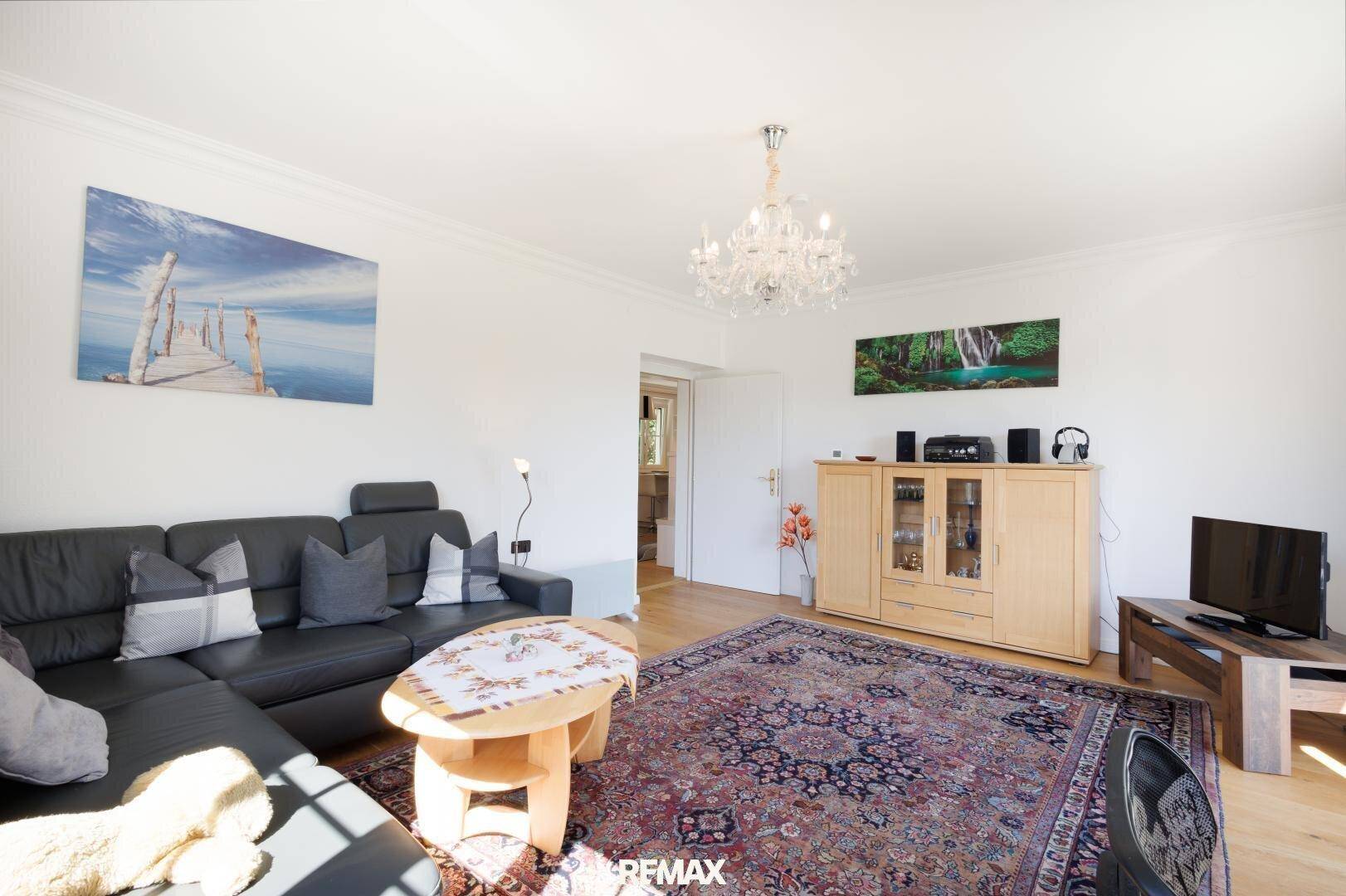 Geräumiges Wohnzimmer mit bequemer Couch, Holzboden und klassischem Kronleuchter an der Decke.