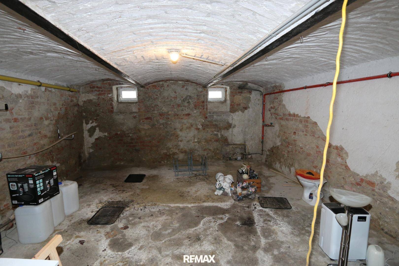 Weiterer Blick in den Kellerraum mit Gewölbedecke, rohen Betonböden und einer einfachen Toilette.