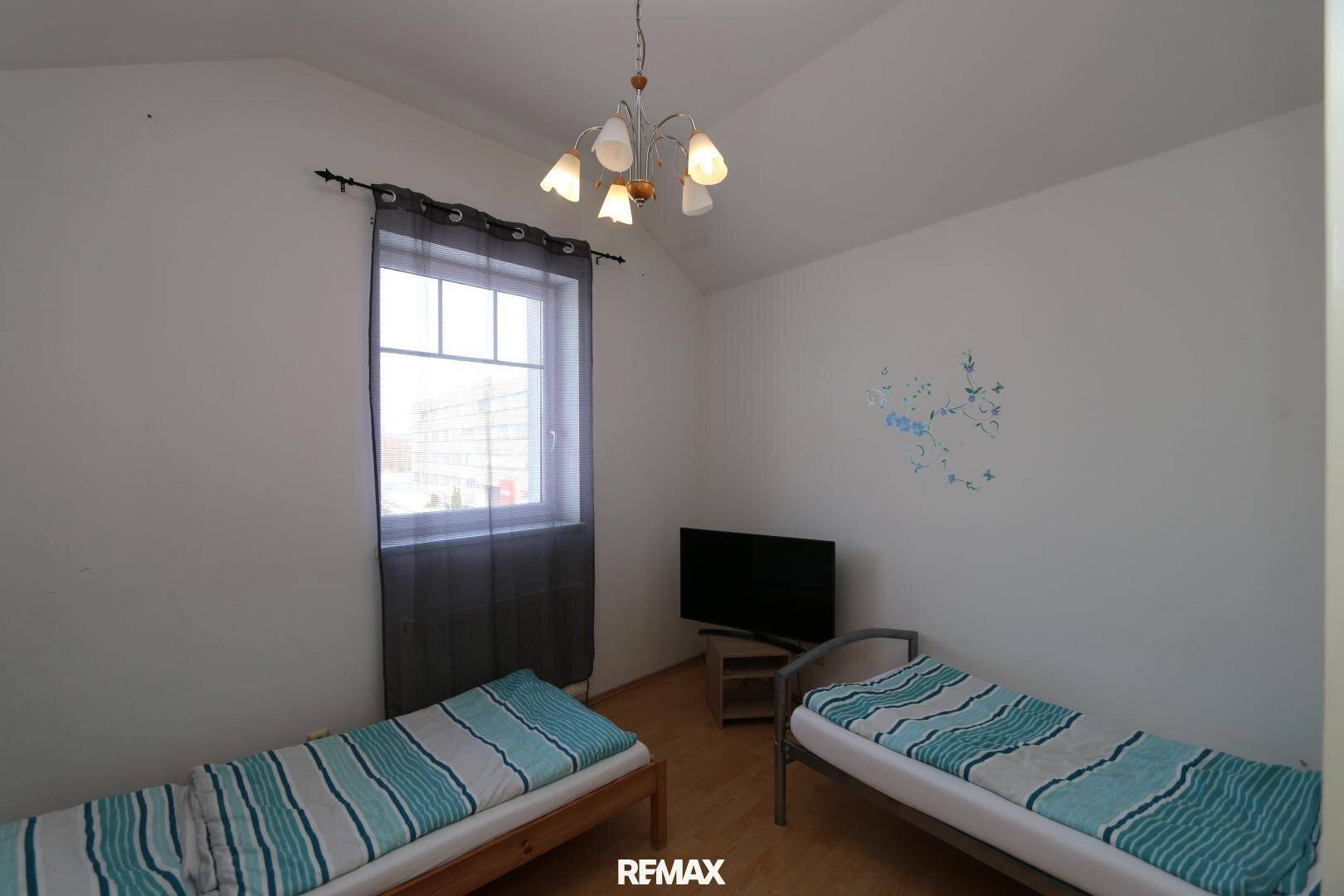 Schlafzimmer mit zwei Einzelbetten, einem Fernseher und einem Fenster, ausgestattet mit Holzfußboden.