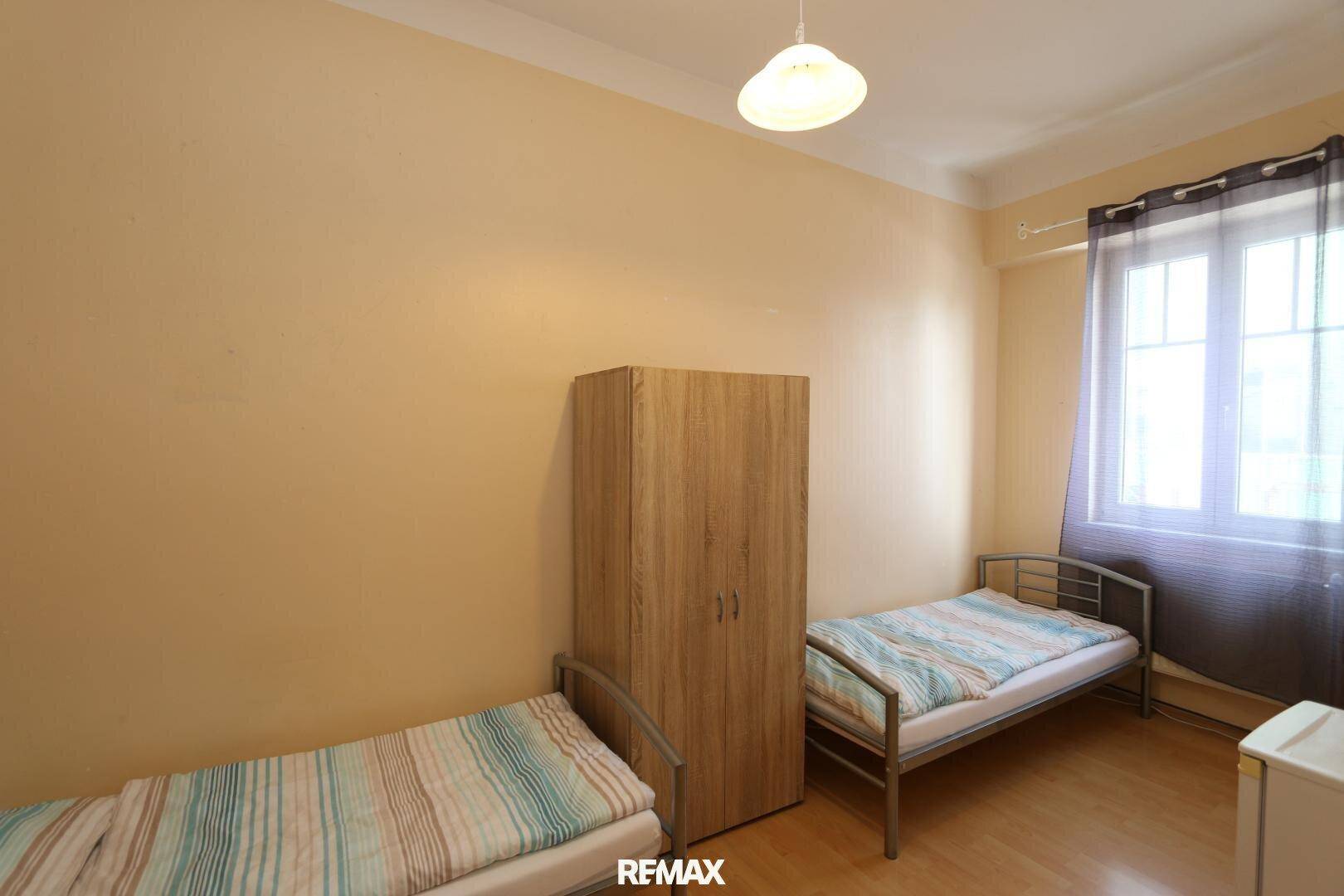 Gemütliches Schlafzimmer mit zwei Einzelbetten und einem Kleiderschrank, helle Wände und Holzfußboden.