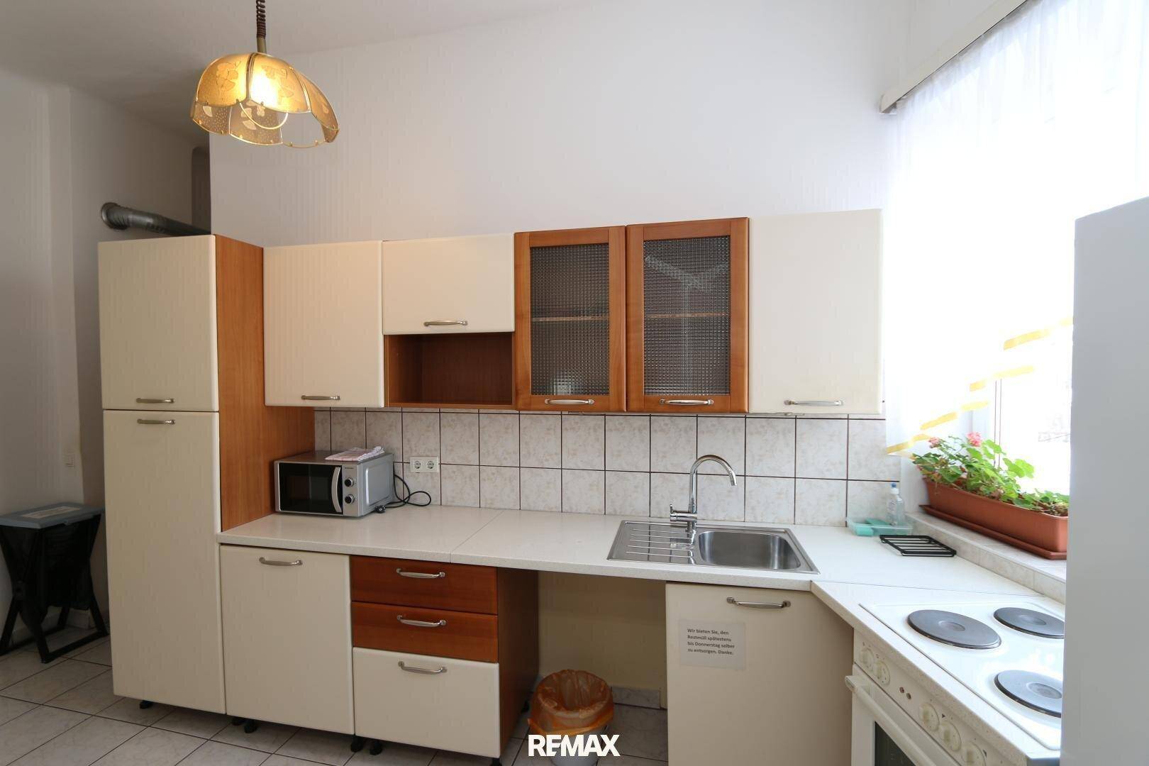 Küche mit hellen Schränken, teilweise mit Glasfronten, Spüle und Herd, gefliestem Boden und Spritzschutz.