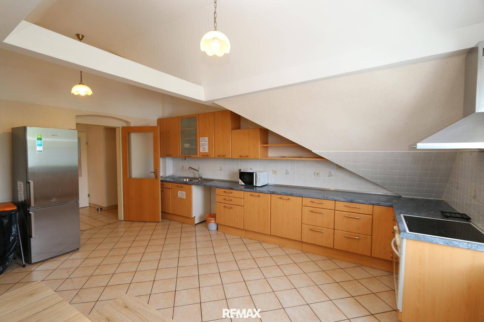 Küche mit Holzschränken, gefliestem Boden, großem Kühlschrank und einer Dachschräge.