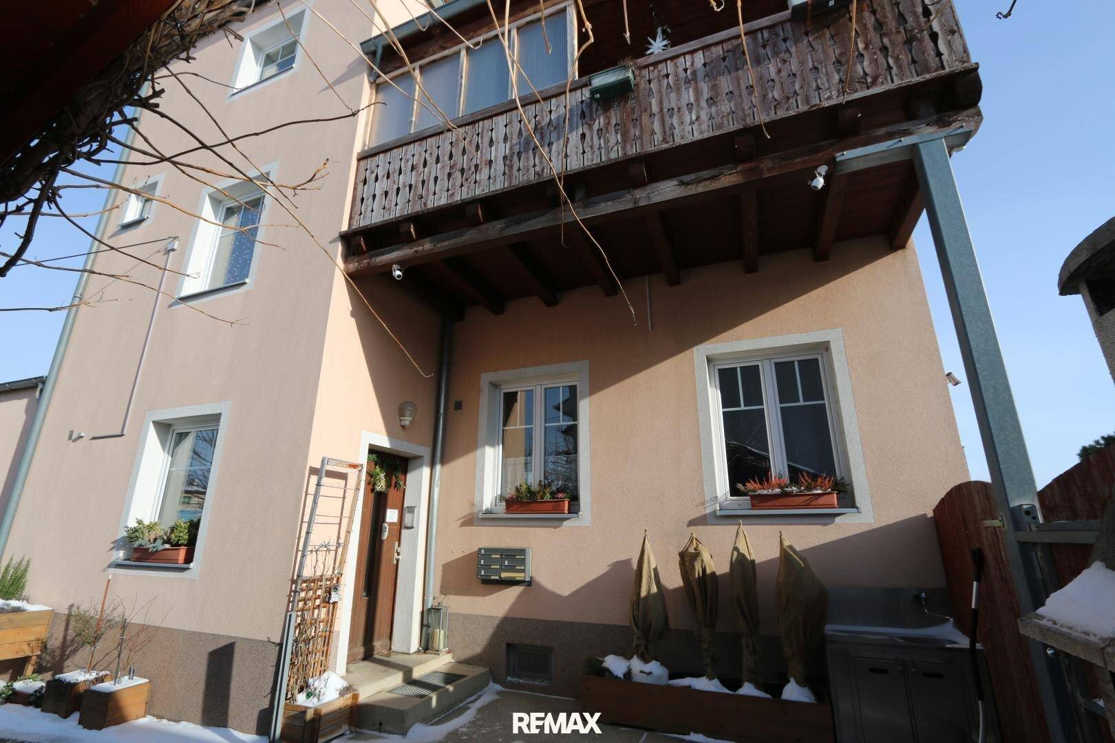 Seitenansicht des Gebäudeeingangs mit einem Holzbalkon darüber, umgeben von Schnee.