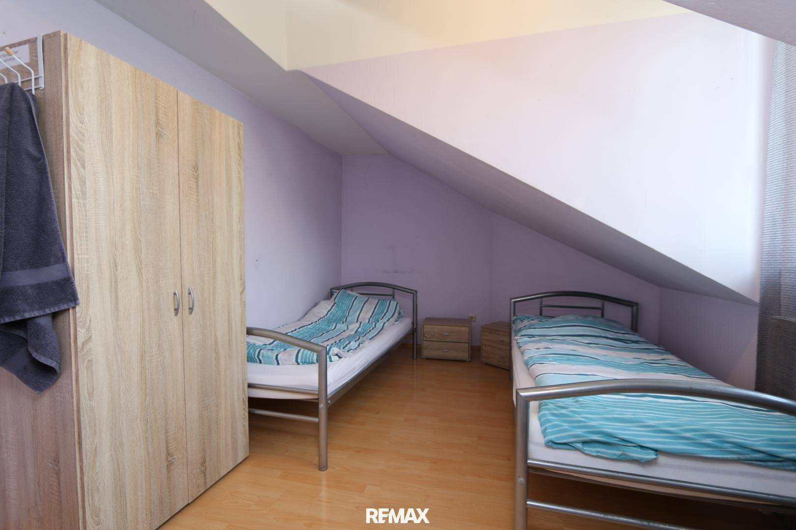 Dachgeschoss-Schlafzimmer mit zwei Einzelbetten und einem Kleiderschrank, schräge Wände und Holzfußboden.