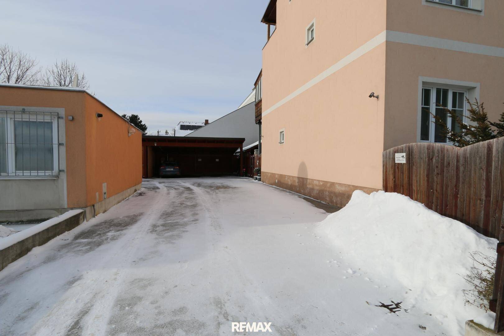Detailansicht der verschneiten Einfahrt und des Carports mit einem geparkten Fahrzeug.