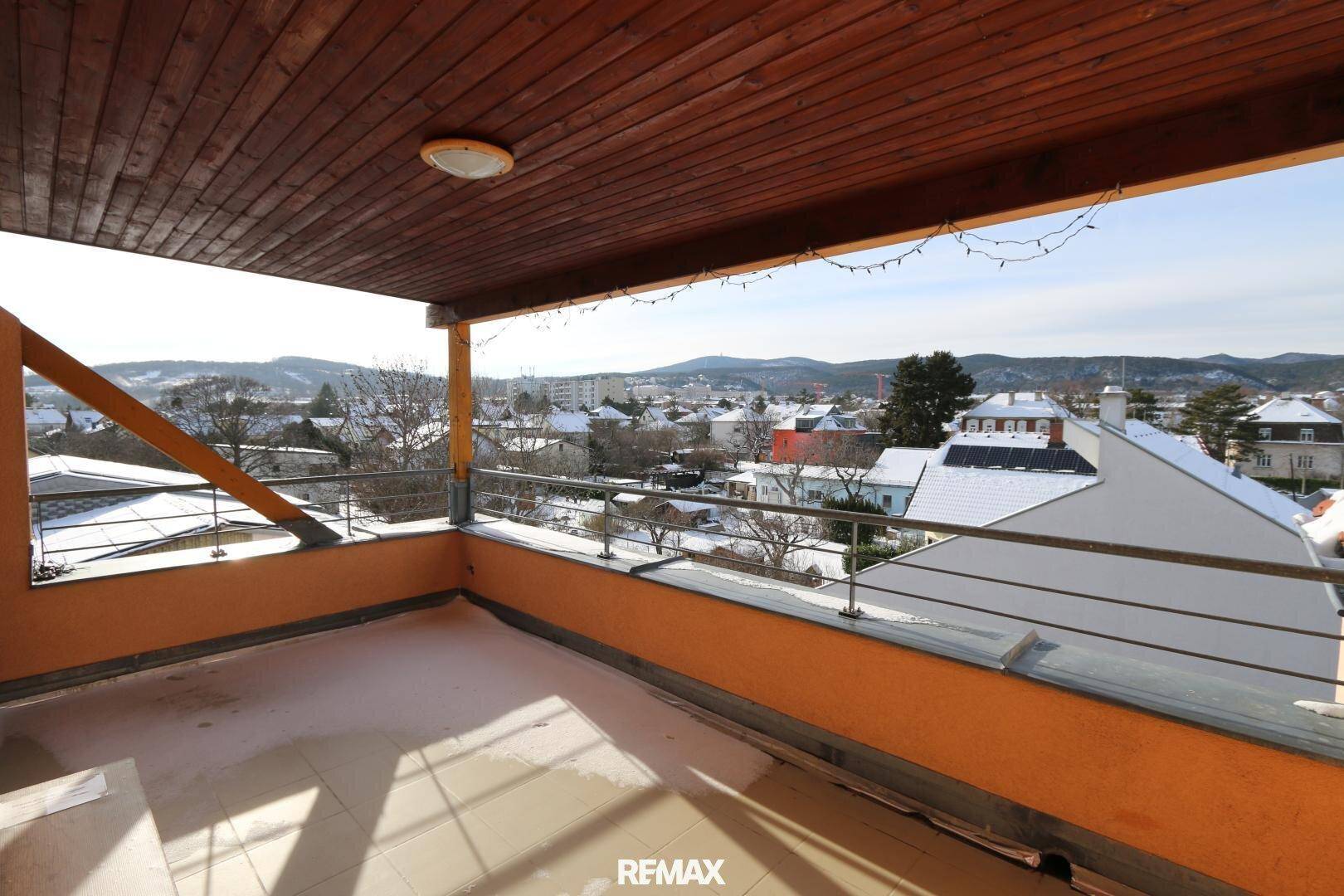 Überdachte Terrasse mit Holzdach und weitem Blick über eine verschneite Stadtlandschaft und Berge.