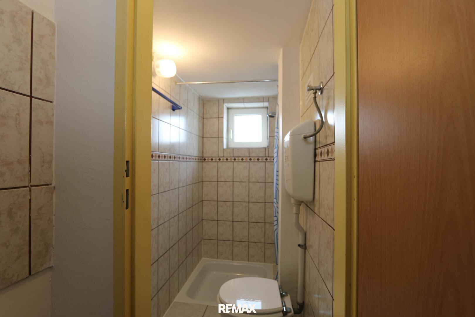Kleines Badezimmer mit WC und Duschbereich, vollständig gefliest und mit einem Fenster ausgestattet.