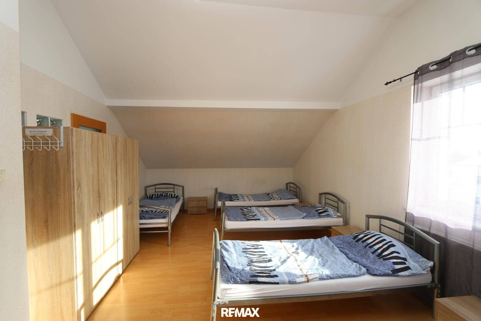 Geräumiges Dachgeschoss-Schlafzimmer mit mehreren Einzelbetten und einem Kleiderschrank, heller Holzfußboden.