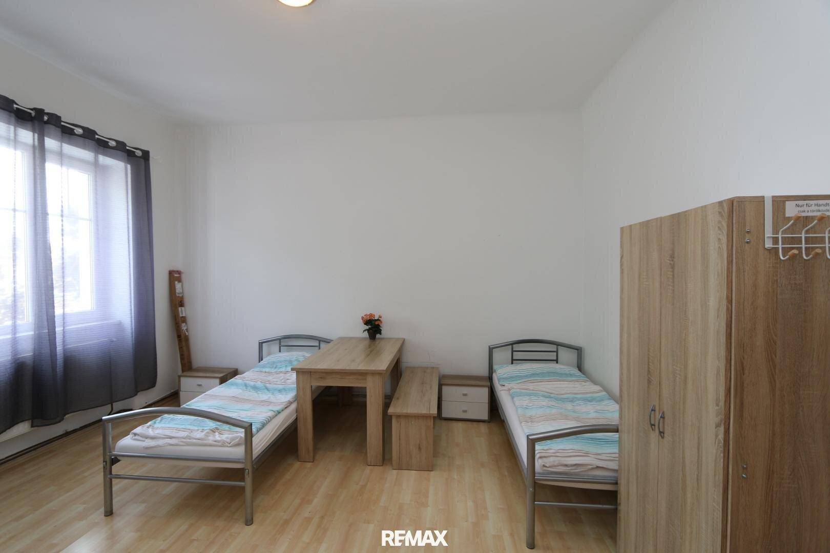 Helles Schlafzimmer mit zwei Einzelbetten, einem Tisch und einem Kleiderschrank, ausgestattet mit Holzfußboden.