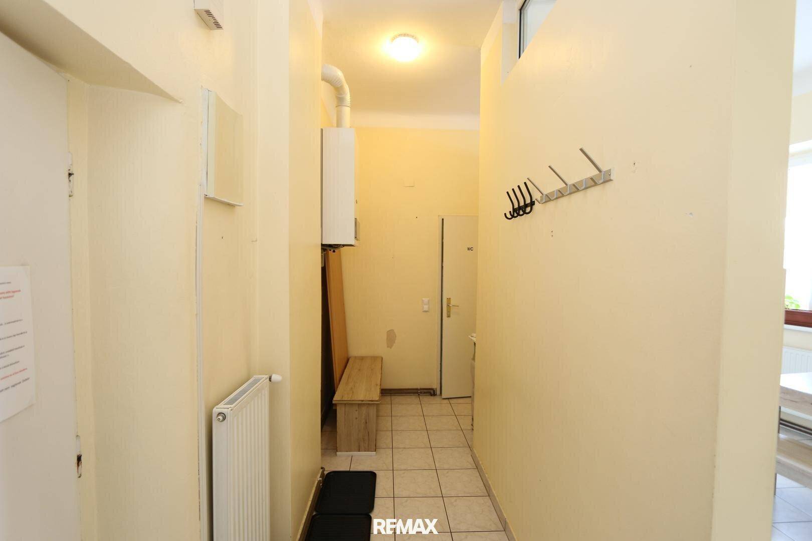 Flur mit gefliestem Boden, hellgelben Wänden und einem an der Wand montierten Heizkessel.