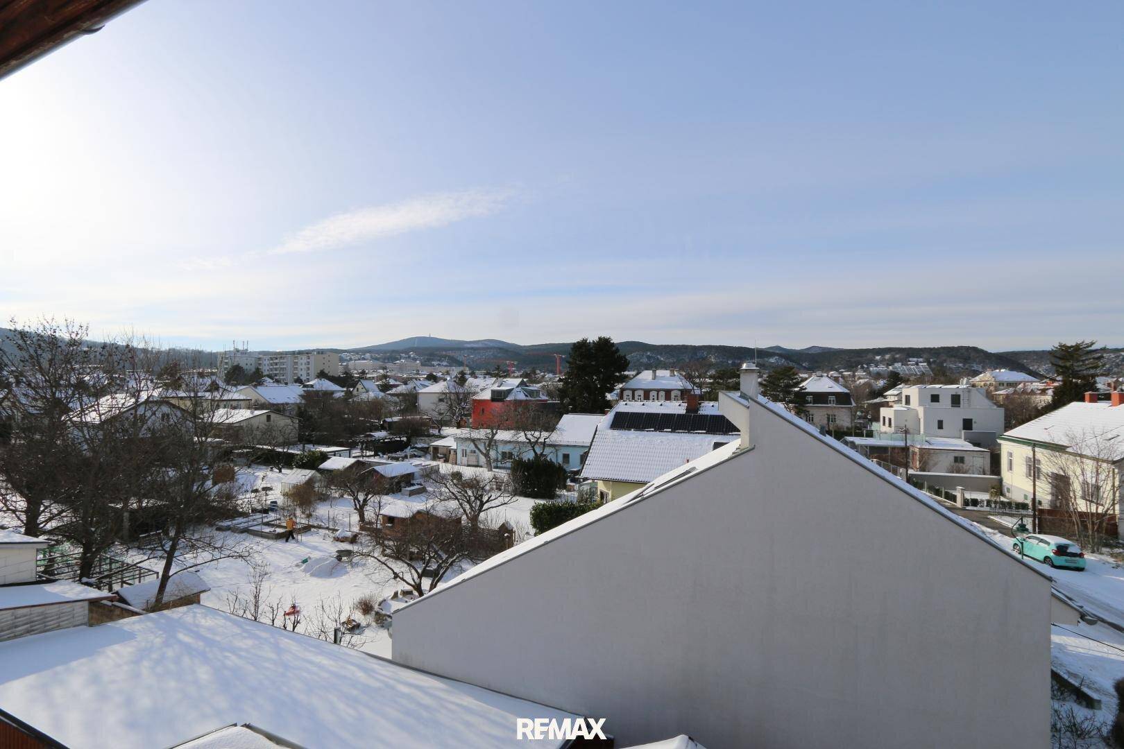 Panoramablick über eine verschneite Stadt mit Häusern und Hügeln in der Ferne unter blauem Himmel.