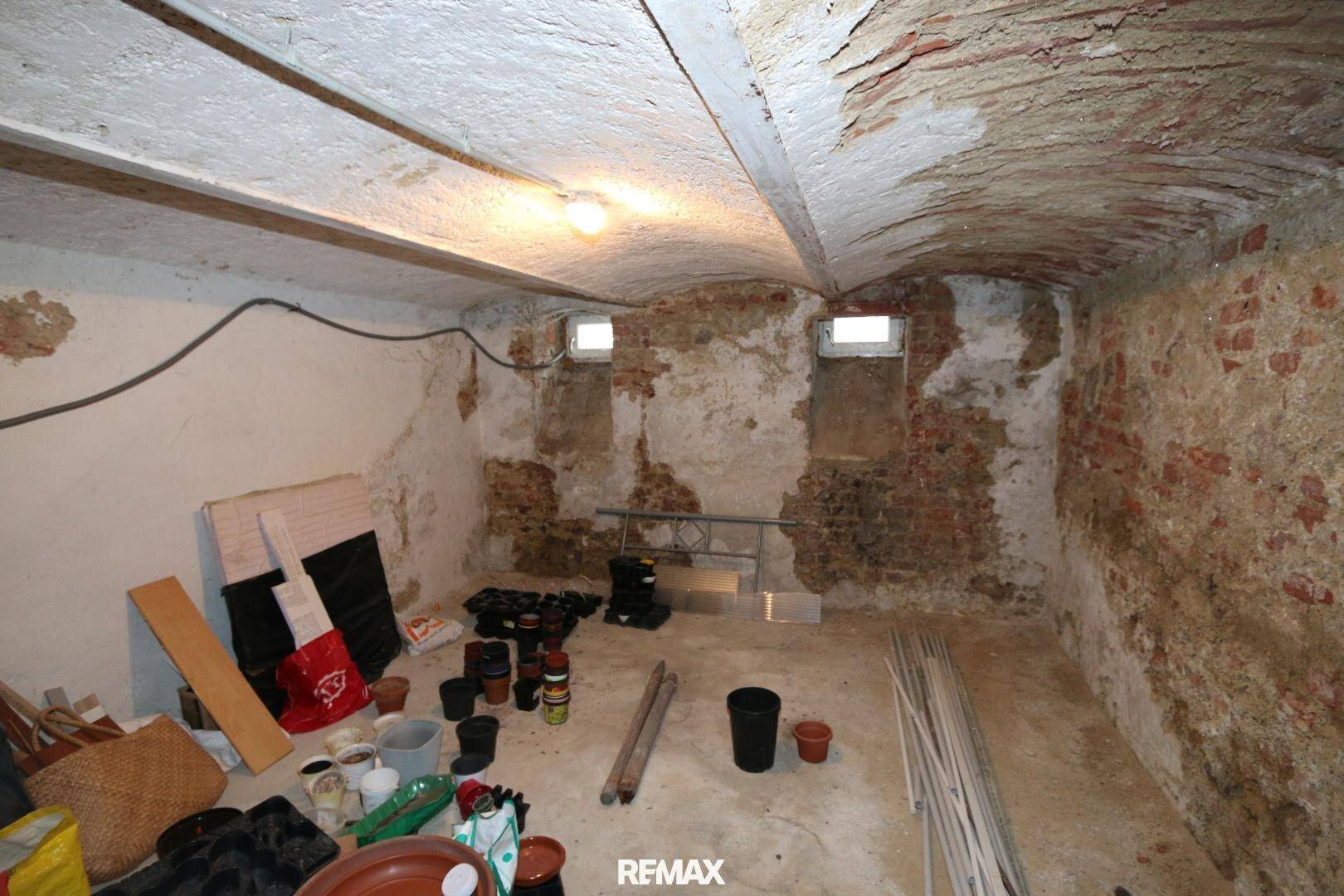 Kellerraum mit unverputzten Ziegelwänden, Gewölbedecke und kleinen Fenstern, als Lagerraum genutzt.