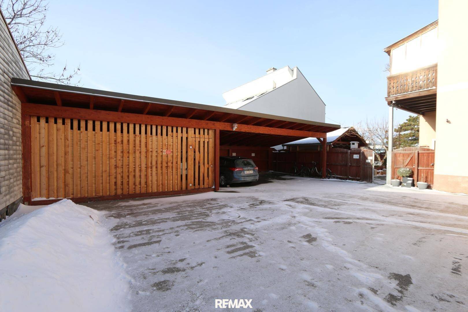 Überdachter Parkplatz oder Carport mit Holzkonstruktion, auf verschneitem Gelände gelegen.