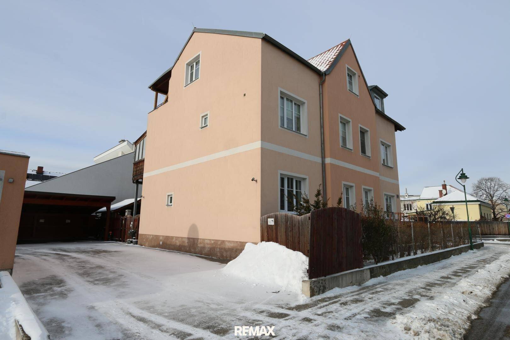 Seitenansicht des Gebäudes mit einer Einfahrt, die zu einem Carport führt, umgeben von Schnee.