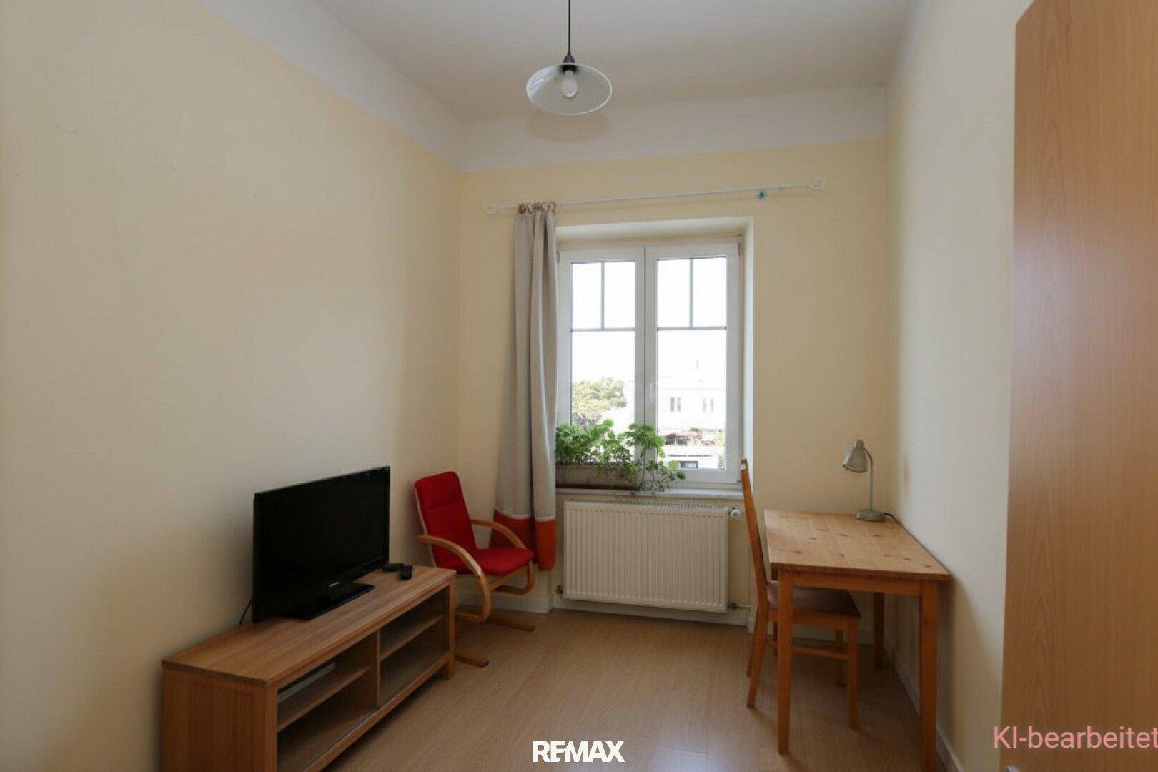 Wohnzimmer mit hellgelben Wänden, Holzboden, TV-Möbeln, einem Schreibtisch und einem Fenster.