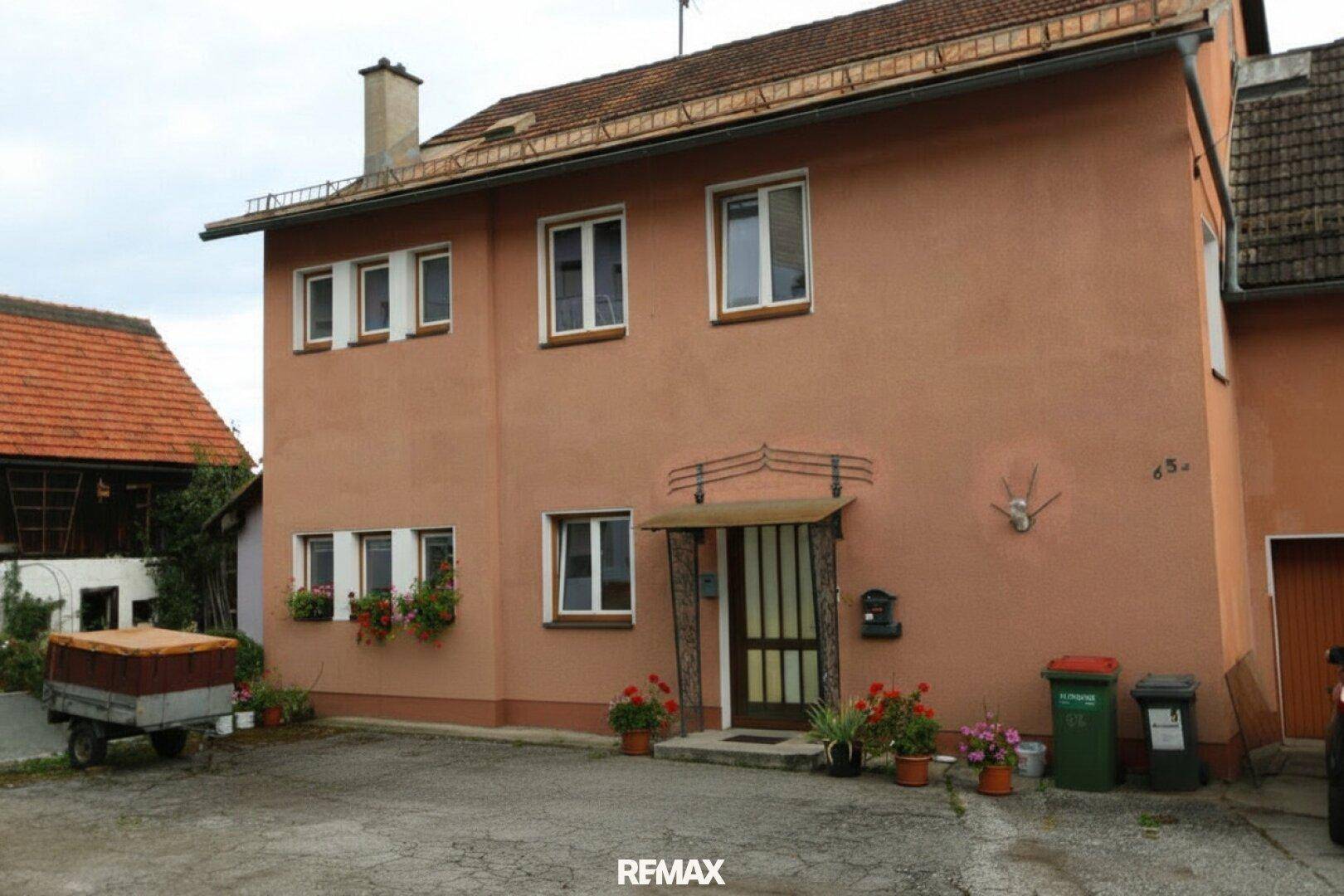 Fassade eines orangefarbenen Hauses mit Blumenkästen an den Fenstern und einem kleinen Vordach am Eingang.
