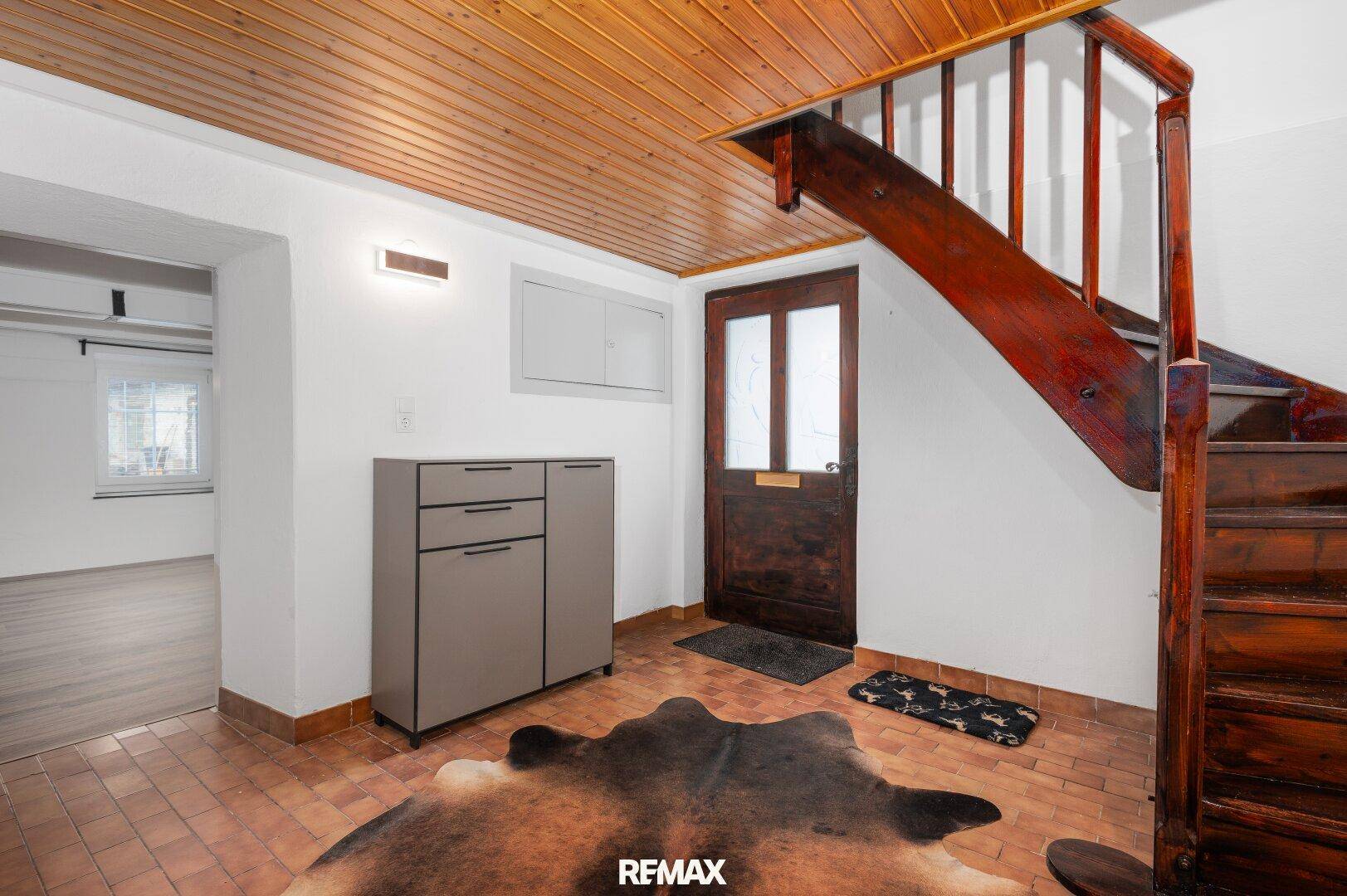 Geräumiger Eingangsbereich mit Terrakotta-Fliesen, Holzdecke und rustikaler Holztreppe.