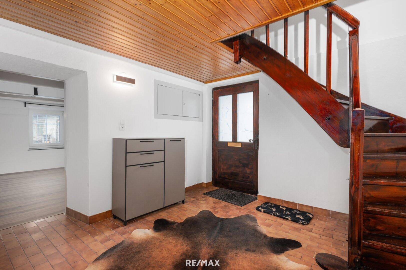 Eingangsbereich mit Holztreppe, Terrakottaboden und Holztür.