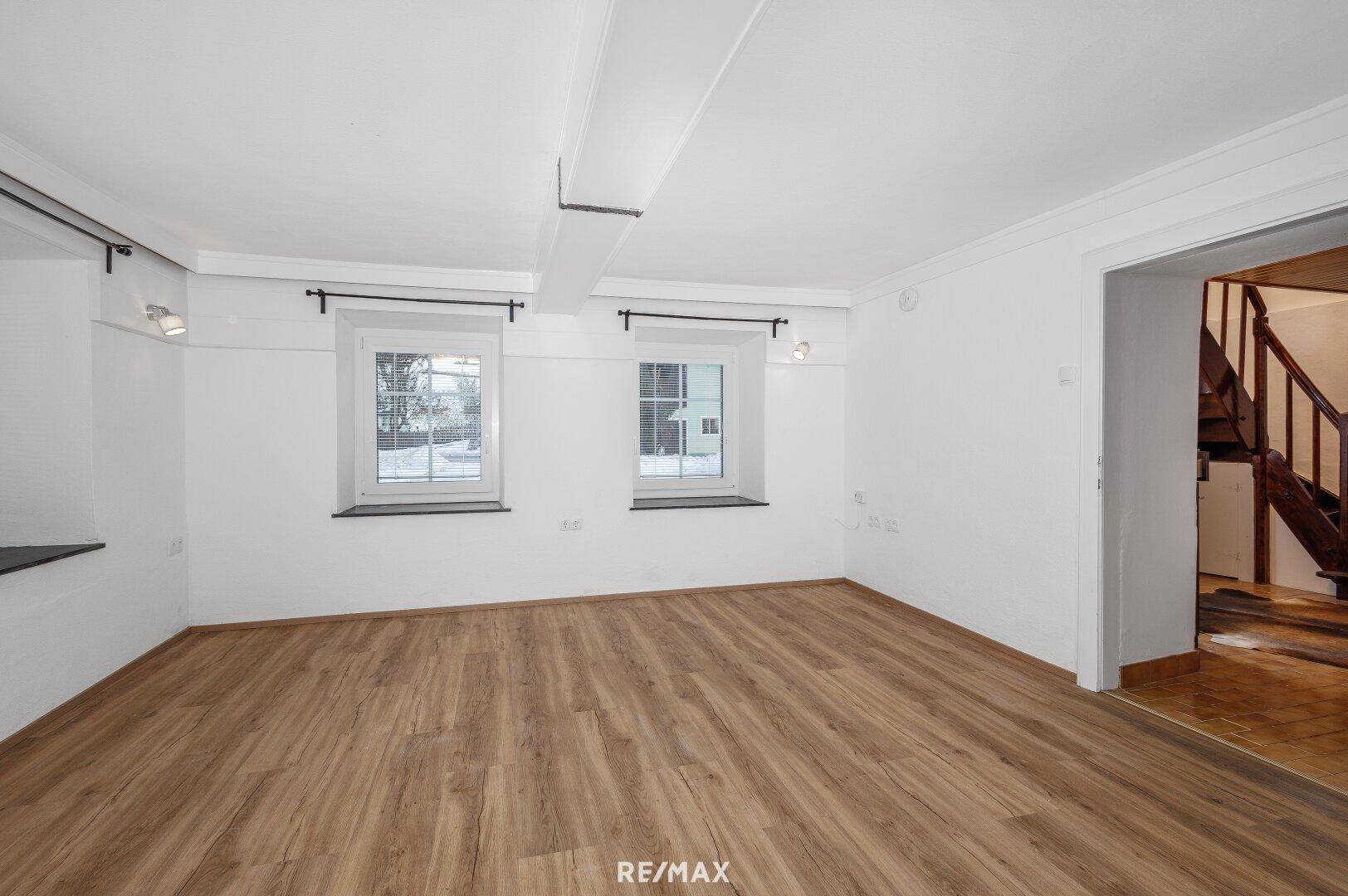 Helles Wohnzimmer mit Parkettboden und zwei Fenstern, die viel Tageslicht hereinlassen.
