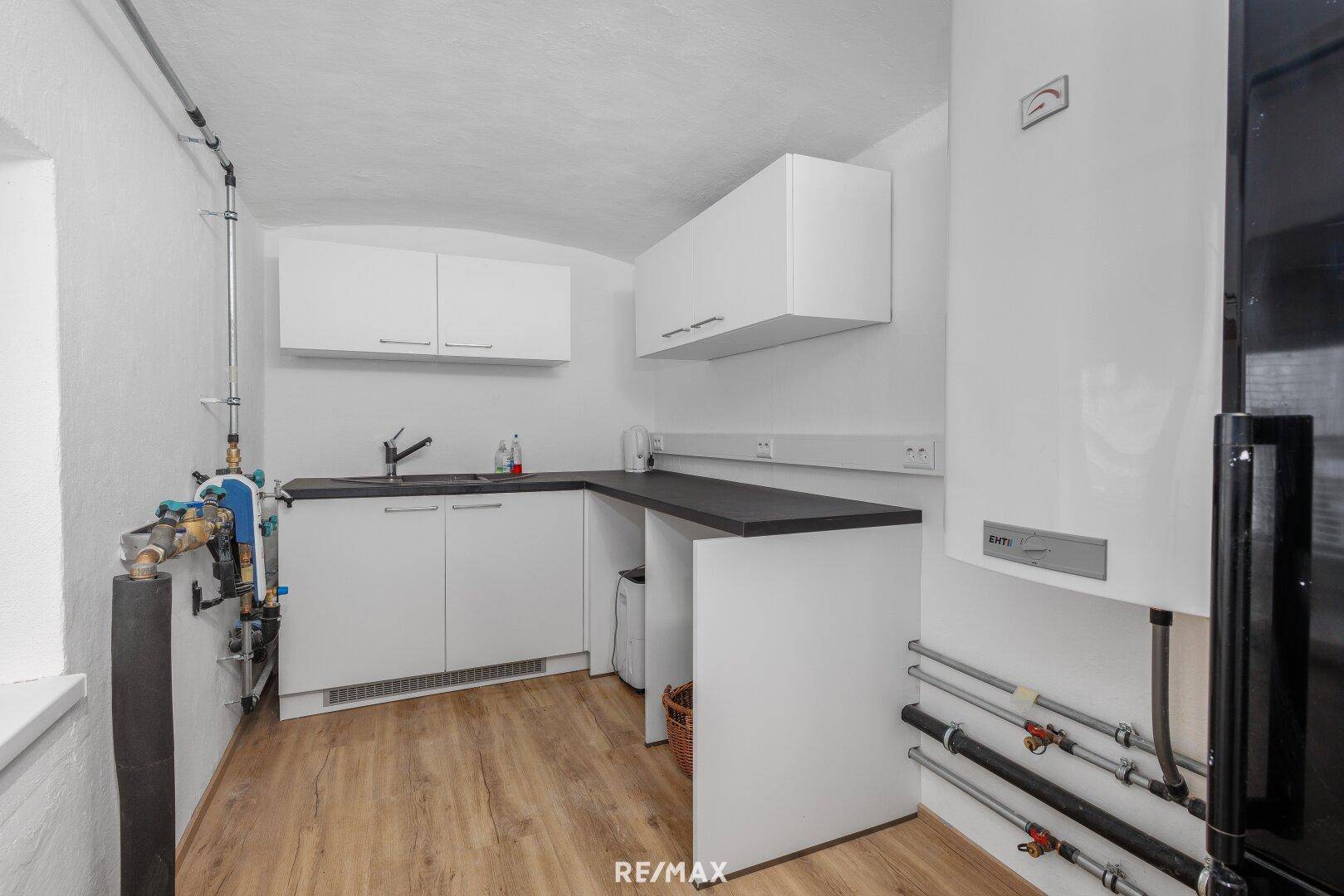 Hauswirtschaftsraum mit kleiner Küchenzeile, Heizungsanlage und sichtbaren Rohren.