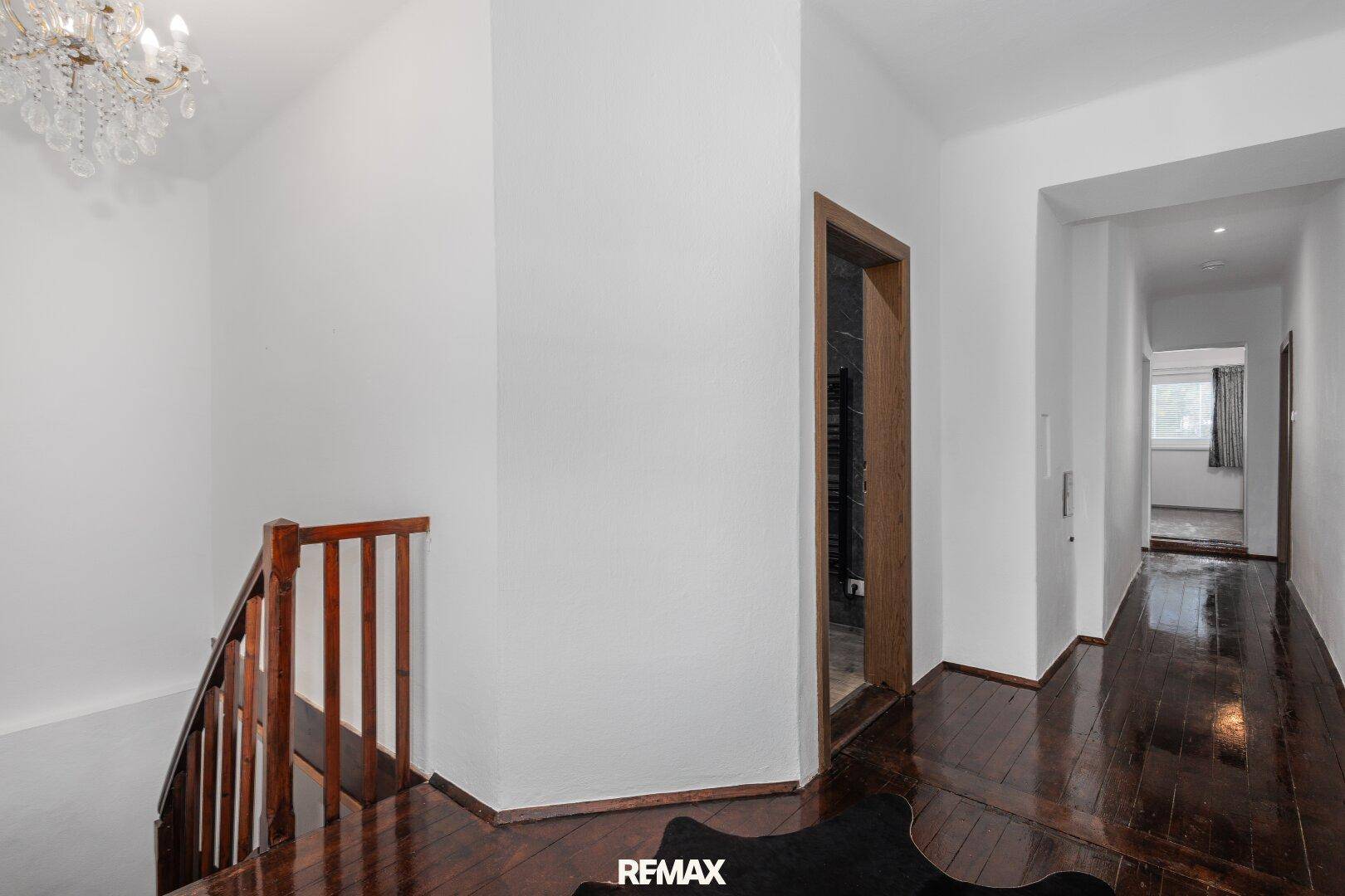 Heller Flur mit Holztreppe, glänzendem Holzboden und einem eleganten Kronleuchter.