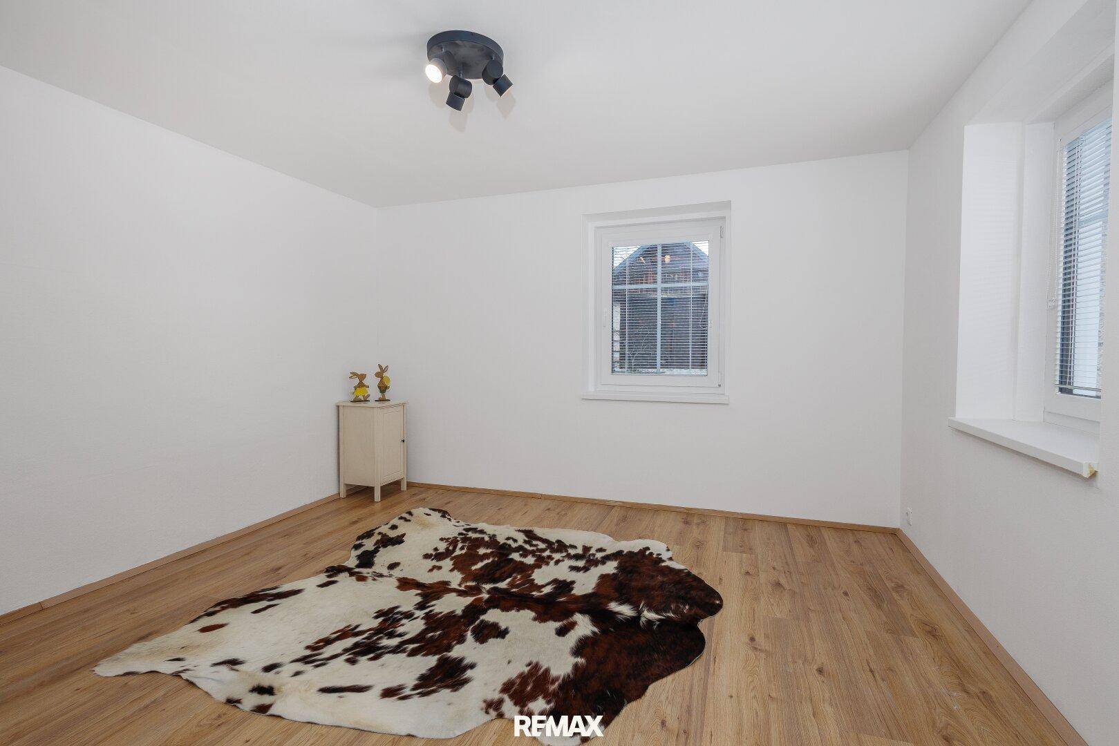 Helles, leeres Zimmer mit Holzboden, weißen Wänden und einem Fenster, bereit zur Einrichtung.